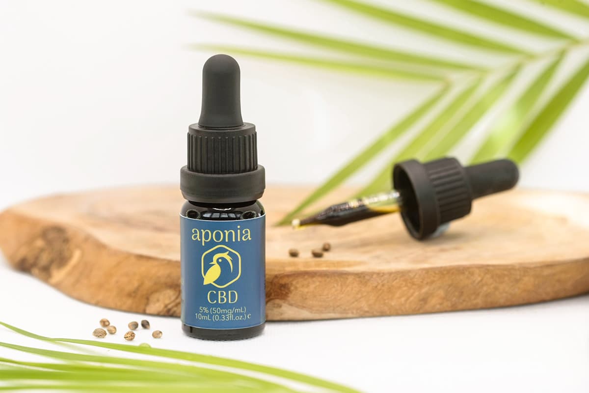 Aponia CBD oil bottle and dropper on wooden board with hemp seeds