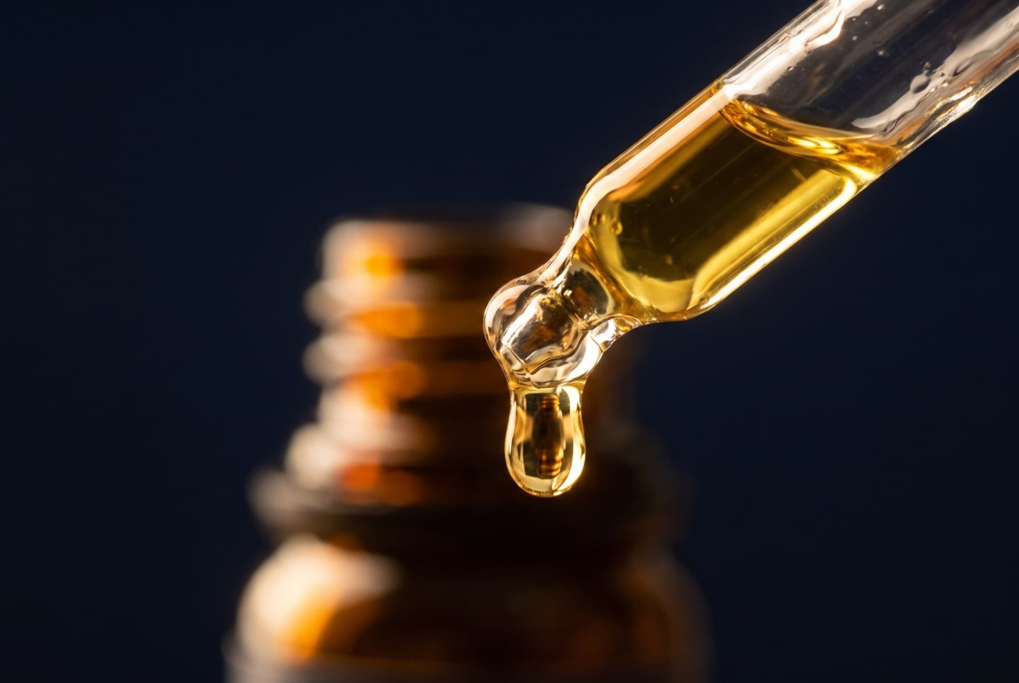 Macro close-up of the Aponia dropper pipette releasing a golden drop of CBD oil